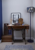 Détail d'angle de chambre montrant une table de machine à coudre Singer avec des ornements vintage et un lampadaire à motifs.