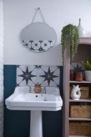 Détail de la salle de bain montrant un lavabo, des carreaux à motifs, un miroir de style vintage et des étagères ouvertes.