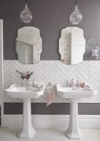 Salle de bain avec double vasque, carrelage blanc à chevrons et miroirs de style vintage.