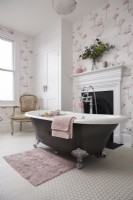 Salle de bain avec baignoire sur pieds, cheminée et papier peint flamant rose.