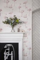 Détail de la salle de bain montrant des robinets de baignoire, une cheminée et un papier peint flamant rose.