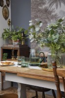 Détail de la salle à manger montrant une table avec de la verrerie, des meubles en bois vintage et des œuvres d'art botaniques.