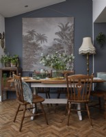 Salle à manger avec mobilier vintage en bois, murs gris foncé et œuvres d'art botaniques.