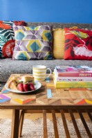 Détail d'une table basse en bois devant un canapé gris avec des coussins colorés dans un salon bleu