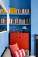 Armoire peinte en rouge recyclée dans un salon bleu avec une étagère à livres au-dessus