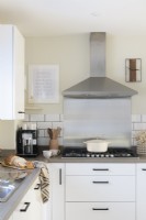 Crédence en acier inoxydable et hotte aspirante derrière une cuisinière à gaz dans une cuisine blanche moderne