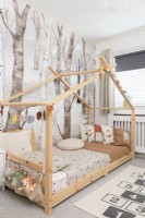 Lit de maison en bois dans une chambre d'enfant devant un papier peint à motifs d'arbres