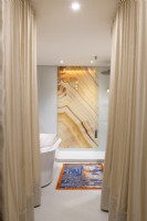 Mur en marbre dans une salle de bains contemporaine avec des rideaux dorés