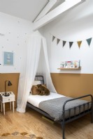 Auvent au-dessus d'un lit simple dans une chambre d'enfant avec un mur peint divisé