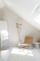 Chaise en osier dans une chambre peinte en blanc avec un long miroir