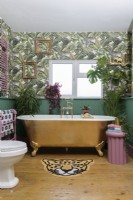 Baignoire dorée dans une salle de bains lambrissée verte avec papier peint à motifs de feuilles de jungle