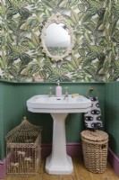Lavabo victorien blanc dans une salle de bains lambrissée verte avec papier peint à motifs de feuilles de jungle