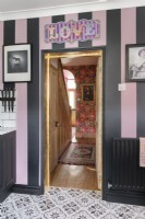 Un mur de cuisine à rayures roses et noires avec vue à travers la porte sur un couloir et un escalier