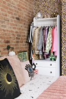 Une armoire et un tiroir blancs à saisir et à emporter dans une alcôve d'angle d'une chambre contre un mur de briques apparentes et de papier peint à imprimé léopard