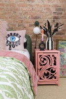 Un mur en briques apparentes dans une chambre avec une table de chevet en rotin peint en rose à côté d'un lit en velours vert