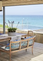 Table à manger et chaises en plein air sur une terrasse en bois avec vue sur la mer