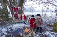 Mère regardant de petits enfants rôtir des guimauves sur un feu ouvert à l'extérieur le jour de Noël. Chaussettes accrochées à la corde après la soirée de patinage