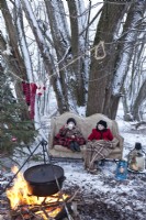 Petit garçon et fille sur un canapé à l'extérieur dans la neige par un feu de camp à Noël