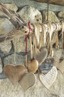 Collection de coeurs du monde entier dans des matériaux et des tailles variés suspendus au bois flotté sur la cheminée du salon.