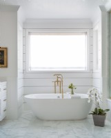 Les raccords dorés ajoutent une touche de luxe à la baignoire. Le blanc pur et la simplicité du cadre confèrent une ambiance de spa à la salle de bain principale.