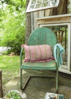 Une chaise de jardin en métal vintage patiné est confortable avec un oreiller et un jeté pour l'observation de la faune.