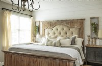 Un mur à déclin et une variété de bois vieillis créent un sens de l'histoire dans la chambre du couple. Le lit king-size est doté d'un cadre de tête de lit en détresse avec un rembourrage capitonné superposé à un panneau de cheminée en bois blanchi à la chaux rustique.