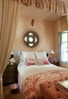 La chambre du couple est habillée d'un assortiment de toiles et de tissus à carreaux avec d'élégantes draperies roses délavées formant une alcôve pour dormir. Au pied du lit, un pouf capitonné cache un téléviseur escamotable.