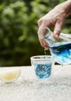 Détail de femme versant de l'eau de couleur bleue dans un verre clair