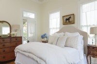 La chambre principale ensoleillée dispose d'une nouvelle tête de lit recouverte de lin beige. Les antiquités, y compris une commode en chêne et des tables d'appoint en bois poli, apportent une sensation de confort d'antan à l'espace reposant.