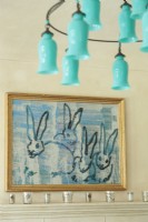 Un lustre en verre bleu sarcelle ajoute une touche de couleur inattendue en hauteur. Une peinture de lapin a inspiré la palette de la pièce.