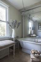 Une grande baignoire antique, un banc recouvert de lin et un miroir surdimensionné donnent à la salle de bain une ambiance élégante.