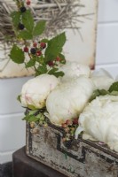 Un petit coffre vintage sert de récipient pour un arrangement frais de pivoines duveteuses et de branches chargées de baies.