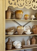 L'armoire antique contient un assortiment de cruches enveloppées d'osier, de pots d'huile d'olive et de plats vintage.