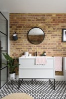 Meuble lavabo blanc avec tiroirs contre un mur en briques apparentes dans une salle de bains moderne