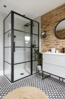 Une cabine de douche crittall dans le coin d'une salle de bains moderne avec un mur en briques apparentes et un sol carrelé à motifs monochromes