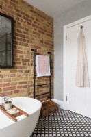 Un porte-serviettes noir dans le coin d'une salle de bain avec des briques apparentes et une porte blanche contre un mur de ciment gris lisse avec un sol carrelé à motifs monochromes
