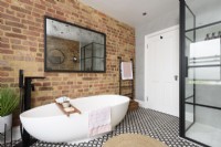 Salle de bains moderne monochrome avec une cabine de douche crittall et une baignoire en céramique en forme de coquille d'oeuf contre un mur de briques apparentes