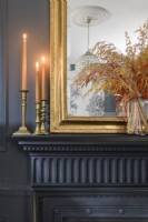 Détail de bougies allumées et de chandeliers et d'un miroir encadré d'or sur une cheminée peinte en noir de l'époque victorienne