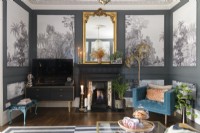 Cheminée victorienne peinte en noir avec miroir doré dans un salon peint en gris avec lambris rempli de papier peint monochrome d'arbres tropicaux