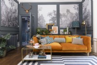 Canapé en velours orange dans un salon gris avec des panneaux remplis de papier peint monochrome à motifs d'arbres tropicaux