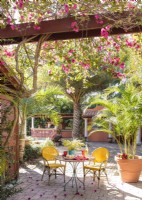 Une table de bistro nichée sous des vignes de bougainvilliers et des palmiers évoque une cour toscane en plein air