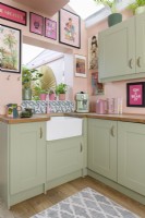Les majordomes blancs évier dans le coin d'une cuisine de style rétro Shaker rose pâle et vert coloré avec une trappe ouverte jusqu'à une véranda