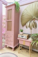 Grande armoire rose recyclée et table de couture vintage peinte en rose récupérée dans une véranda rose avec lampe de table en fougère tropicale dorée
