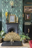 Cheminée victorienne noire avec papier peint à motifs vert art déco et pare-feu décoratif en forme d'éventail paon doré