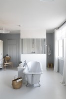 Baignoire autoportante au centre d'une grande salle de bains blanche et grise