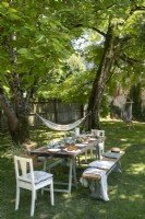 Jardin de campagne avec table à manger dressée pour le déjeuner à l'ombre des arbres