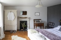 Une chambre de campagne luxueuse et douce avec une armoire peinte en blanc, un lit recouvert d'un jeté violet et un lavabo surmonté de marbre.