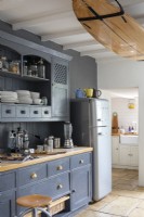Maison de Sally et John Biddle à Cornwall, armoires de cuisine peintes en bleu et réfrigérateur Smeg moderne, avec planche de surf fixée aux poutres du plafond