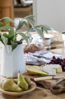 Détail de la table de cuisine, avec feuillage dans un vase, fromages mélangés, poires et raisins