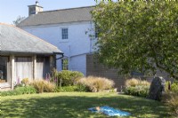Maison de Sally et John Biddle à Cornwall, l'extérieur montrant un joli jardin d'été avec des granges et une maison en pierre